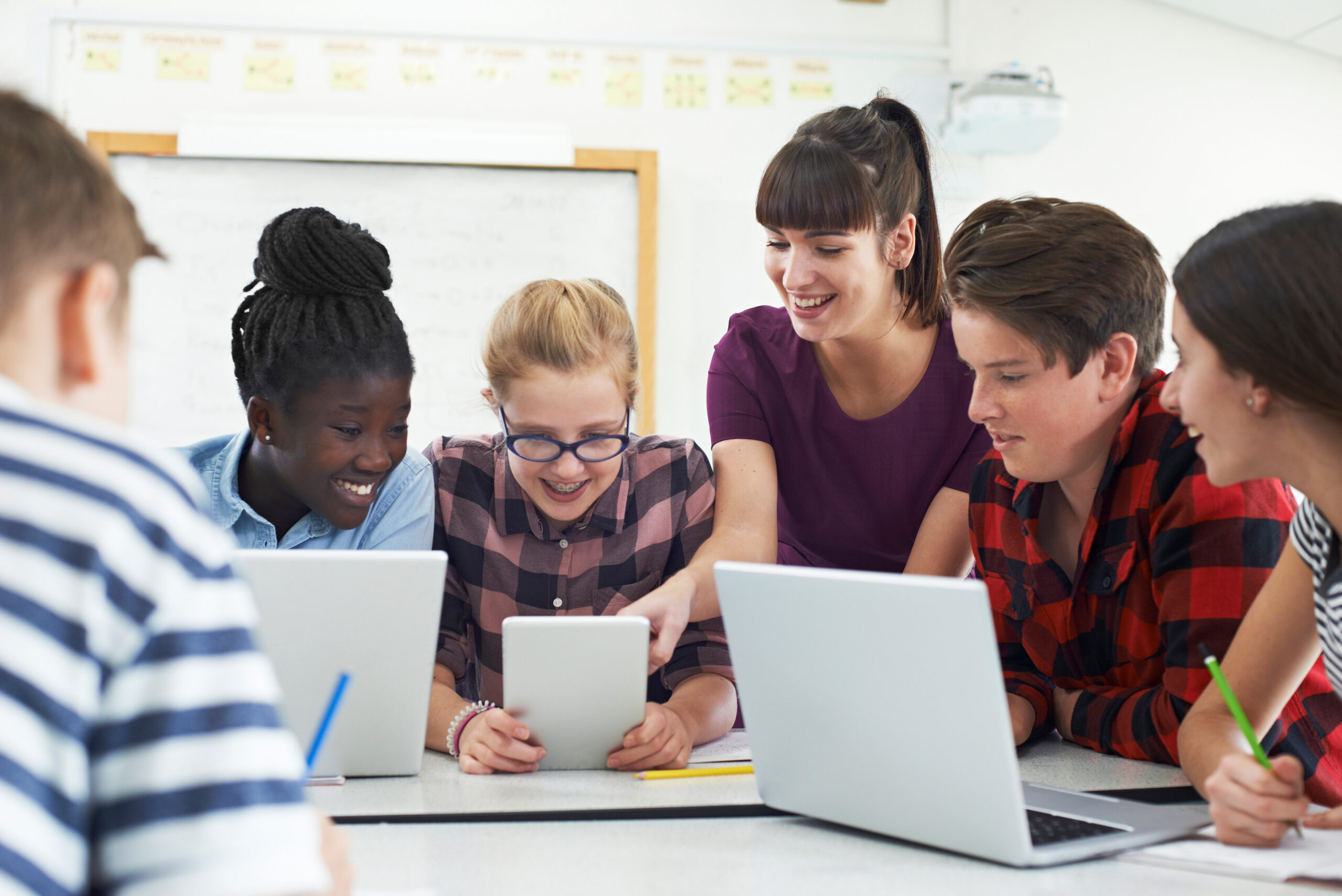 Teacher interacting with teenage students working on laptops