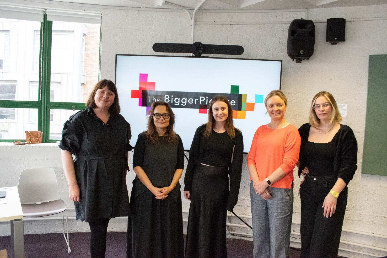 The image shows five women standing together in front of a screen displaying the logo for "The Bigger Picture." The group appears to be part of an event or presentation, possibly related to discussions on AI or technology. All five women are smiling, and the setting is a well-lit room with large windows in the background. One of the women is wearing a bright orange top, while the others are dressed in black and dark clothing. The screen behind them includes colorful geometric shapes around the logo, giving a modern and creative feel to the event.

From the left: Emma Clarke, Tania Duarte, Faye Murphy, Helen Sheridan, Nic Flanagan