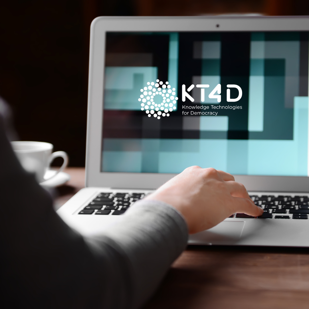 Person sitting at a table using a laptop with KT4D logo as the laptop's screensaver.