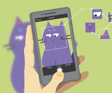 An illustration showing a hand holding a smartphone with its camera app open, capturing an image of a cartoon purple cat. The camera screen displays the cat framed with a square outline, and several facial features—such as the eyes, ears, and nose—are highlighted with smaller boxes and connected by thin lines, illustrating an AI recognition process. The cat is slightly blurred in the background outside the phone screen, emphasising the focus on the camera's view.